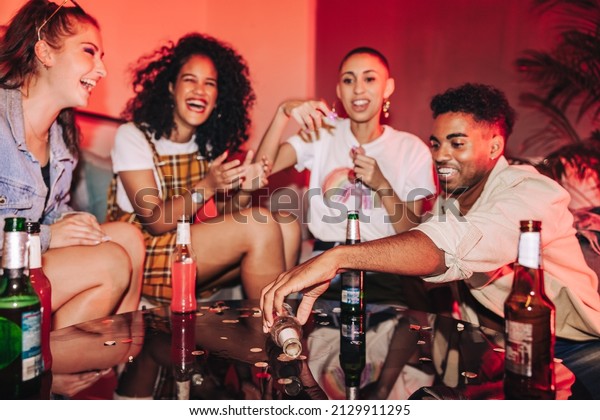 Friends
playing spin the bottle at a house party. Group of generation z
friends laughing and having a good time in neon light. Cheerful
friends having fun together on the
weekend.