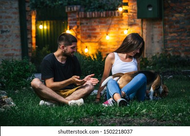 Friends Playing With Their Dog Outdoor At Home Backyard. Night Scene