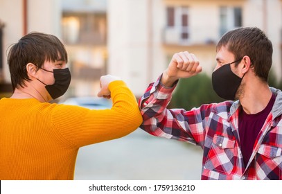 Friends In Protective Medical Mask On His Face Greet Their Elbows In A Quarantine. Elbow Bump. Friends Medical Mask. People Wear Face Mask Outside. Friends Bump Elbows Outdoors. Coronavirus Epidemic.