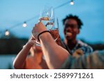 Friends raising glasses of sparkling wine at a rooftop party, celebrating together under string lights against a twilight sky