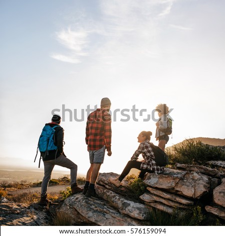 Friends relaxing on a rock in countryside. Young people on hike.