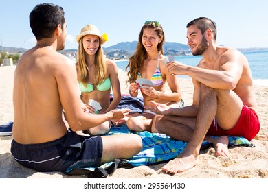 Friends Resting On A Beach Sitting On Towel And Playing Poker Card Game