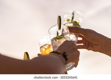 Friends rising cocktail glasses for a celebratory toast against the sky in the summer - Shutterstock ID 2053245641