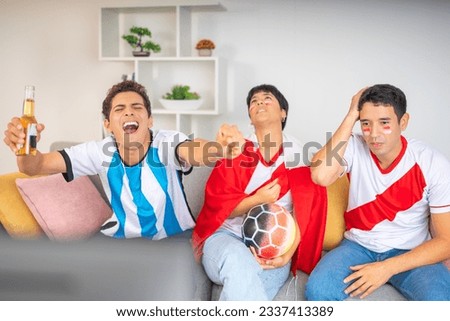 Friends from rival teams excitedly watching a soccer game, in the apartment