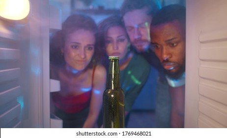 Friends Run Out Of Beer. View Of Four Diverse Friends Opening Steamy Fridge Finding One Last Bottle Of Beer. Young Multiracial People Lack Alcohol At Home Party