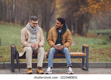 Friends, a senior and a young man sit in the park on a bench and talk in the autumn park. - Shutterstock ID 2223480831