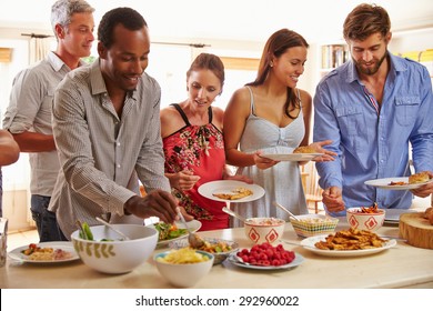 Friends Serving Themselves Food And Talking At Dinner Party