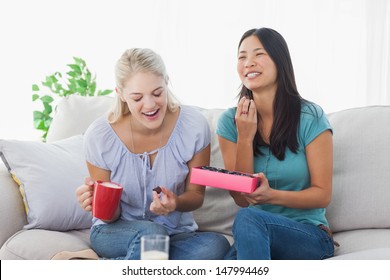 Friends Sharing A Box Of Chocolates And Laughing At Home On The Couch