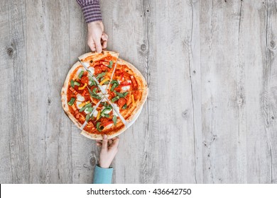 Friends sharing a delicious pizza on a rustic table, they are holding a slice, top view