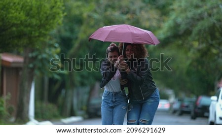 Friends sharing umbrella together during rainy day