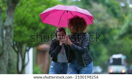 Friends sharing umbrella together during rainy day