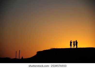 Friends silhouetted by a stunning hilltop sunset, creating lasting memories - Powered by Shutterstock