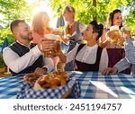 Friends sitting in beer garden or oktoberfest with beer glasses toasting to each other in Bavaria, Germany