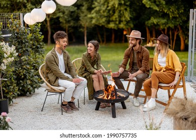 Friends sitting by a fireplace, having great summertime at backyard near the forest. Barbecue in close company in nature