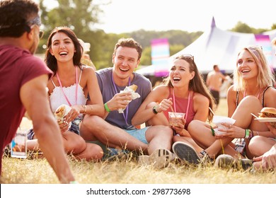 Friends sitting on grass and eating at music festival
