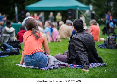 Friends Sitting On The Grass, Enjoying An Outdoors Music, Culture, Community Event, Festival.