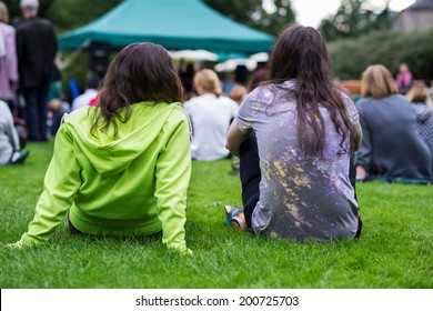 Friends Sitting On The Grass, Enjoying An Outdoors Music, Culture, Community Event, Festival.