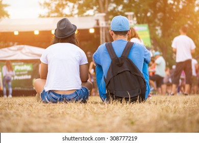 Friends Sitting On The Grass, Enjoying An Outdoors Music, Culture, Community Event, Festival