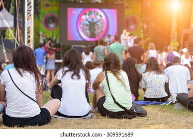 Friends Sitting On The Grass, Enjoying An Outdoors Music, Culture, Community Event, Festival