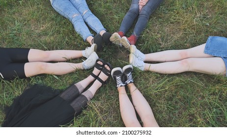 Friends Are Sitting On The Grass With Their Legs Joined In A Circle.