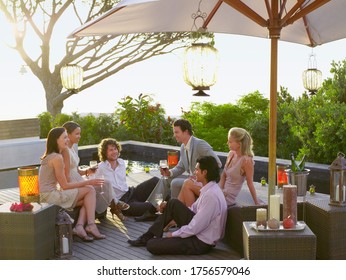 Friends Sitting On Porch Drinking And Socialising Under Umbrella