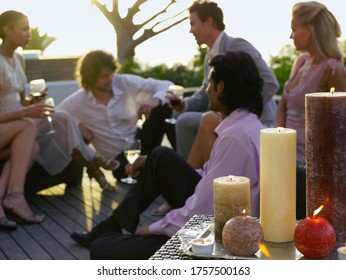 Friends Sitting On Porch Drinking And Socialising Near Candle Arrangement