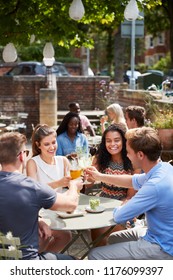 Friends Sitting At Table In Pub Garden Making Toast Together