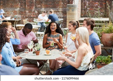 Friends Sitting At Table In Pub Garden Enjoying Drink Together