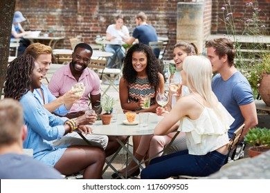 Friends Sitting At Table In Pub Garden Enjoying Drink Together