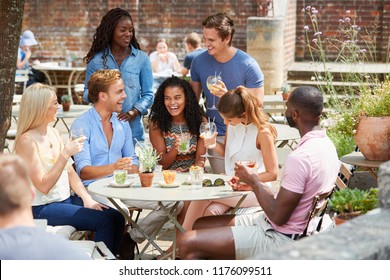 Friends Sitting At Table In Pub Garden Enjoying Drink Together