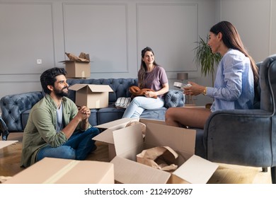 Friends sitting and talking in their new apartment while unpacking their things from cardboard box. - Shutterstock ID 2124920987