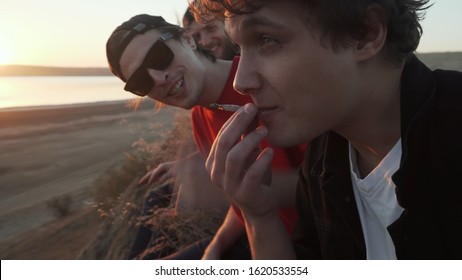 Friends Skateboarders Smoking Joint With Weed At Seashore At Sunset