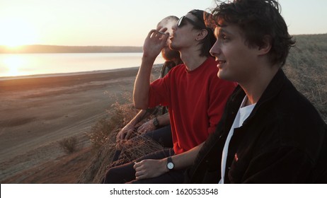 Friends skateboarders smoking weed at seashore at sunset