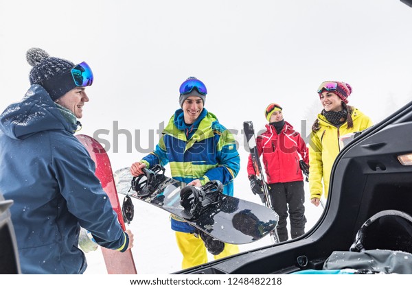 Friends with ski\
and snow board unloading stuff from the car. Winter sport scene\
with a group of young people wearing skiing clothes and smiling.\
Sport and lifestyle\
concepts