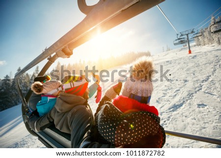 friends skiers and snowboarders on ski lift in the mountain at winter vacations back view