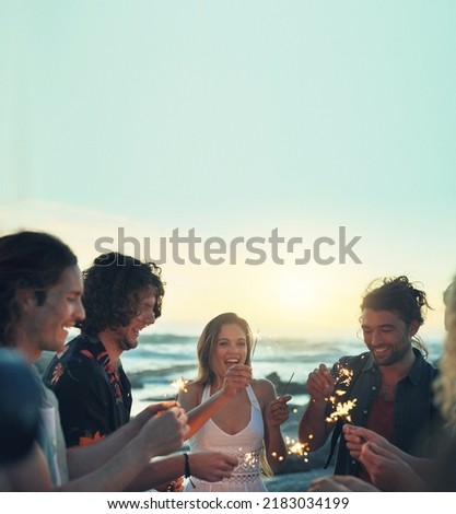 friends with sparklers celebrating new years eve on beach at sunset