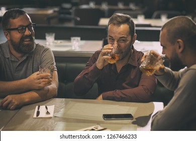 Friends Spending Time Together In Bar After Work. Man In Spectacles Smiling And Looking At His Friends. Two Men Drinking Alcohol Beverages, Delicious Scotch, Rum Or Brandy.