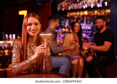 Friends spending time together in bar. Beautiful woman with fresh alcoholic cocktail at table, space for text - Powered by Shutterstock