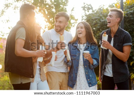 Friends spending time together. Group of young people having fun, eating hot dogs telling jokes and laughing.