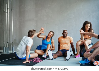 Friends in sportswear high fiving and laughing together while sitting on the floor of a gym after a workout - Powered by Shutterstock