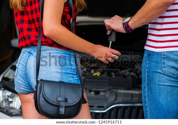 Friends standing in front of a car and the guy is\
giving his keys to the\
girl