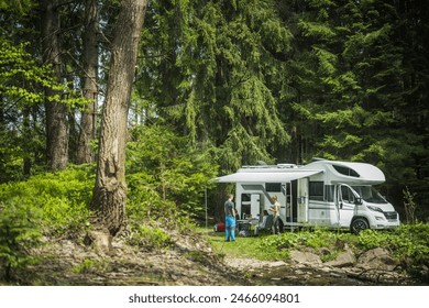 Friends standing in front of a parked camper van, looking at each other. The camper is parked by a serene lake, with trees in the background. - Powered by Shutterstock