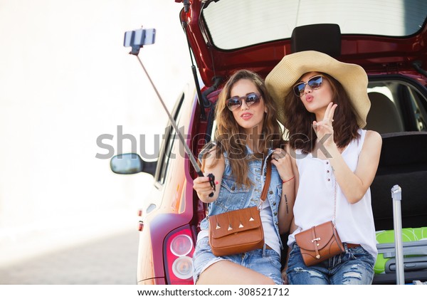 friends\
taking a selfie in the back of the car before leaving for\
vacations. Two women taking self portraits sitting in back car with\
suitcases. Vacation, trip concept. Road travel.\
