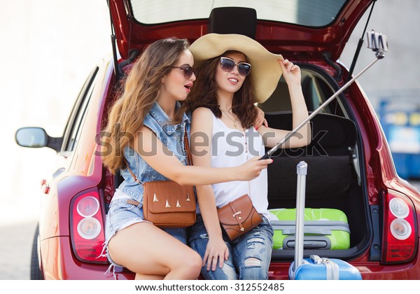 friends\
taking a selfie in the back of the car before leaving for\
vacations. Two women taking self portraits sitting in back car with\
suitcases. Vacation, trip concept. Road\
travel.