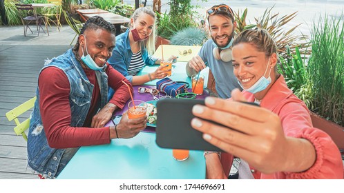 Friends taking selfie in a bar restaurant with face mask on in coronavirus time - Young people having fun with drinks and snacks outside with new rules after virus break 