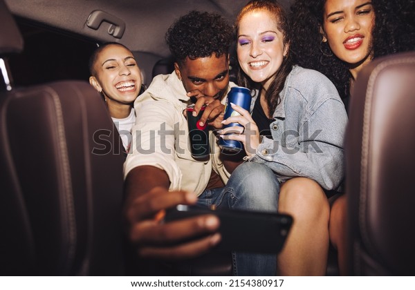 Friends taking a selfie\
inside a car at night. Group of happy young friends smiling\
cheerfully while posing for a group photo. Carefree friends taking\
a ride home after a\
party.