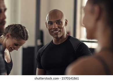 Friends talking and laughing together in gym. Group of four multiethnic people relaxing in conversation. Black sweaty guy and young women talking to each other while resting after intensive training. - Powered by Shutterstock