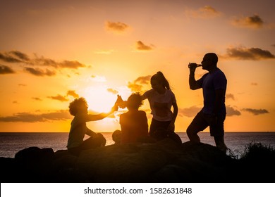 Friends toasting with bottles of beer, beautiful sunset on the ocean in background. Modern family cheering with drinks, amazing orange sky with clouds over the sea. Group of people enjoying together - Powered by Shutterstock