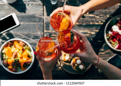 Friends toasting each other with aperol spritz cocktails at the dinner table, top view