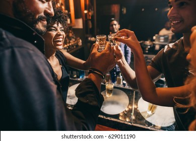 Friends toasting each other with shots of vodka as they enjoy a relaxing night out together at the pub. Group of friends together having fun